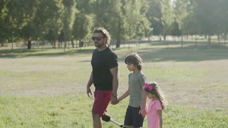 Side-view-of-dad-with-artificial-leg-strolling-with-kids-in-park
